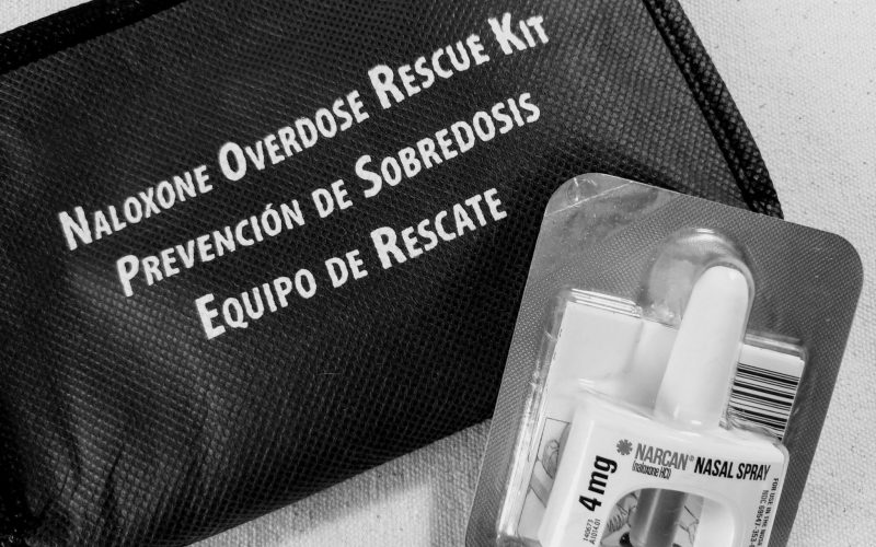 A black and white photo of a zipper bag that says "Naloxone overdose rescue kit" with a single dose of nasal spray Narcan
