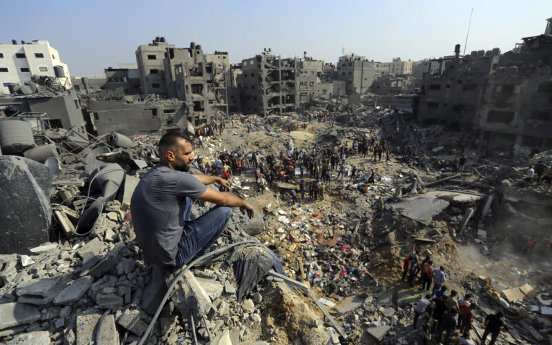 A man sits on the rubble as others wander among debris of buildings that were targeted by Israeli airstrikes in Jabaliya refugee camp, northern Gaza Strip, Wednesday, Nov. 1, 2023. A new U.N. report paints a stark picture of the devastating collapsing Palestinian economy after a month of war and Israel’s near total siege of Gaza. (AP Photo/Abed Khaled, File)