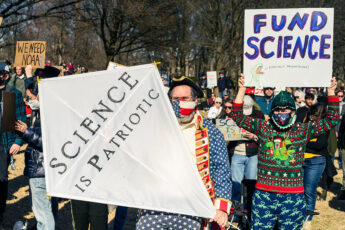 Protestors in colorful gear hold up "Science is Patriotic" and "Fund Science" posters at the Stand up For Science protest in Washington DC in March 2025.
