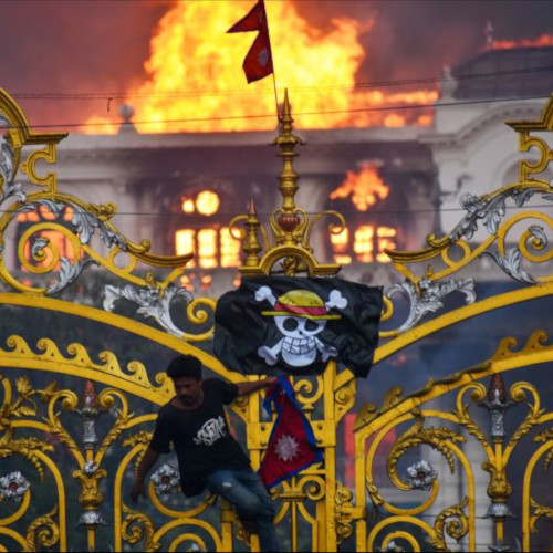 a photo of someone climbing the gilded gates of the Nepalese parliament building, hanging a flag with a skull and crossbones and wearing a straw hat, with the parliament burning in the background