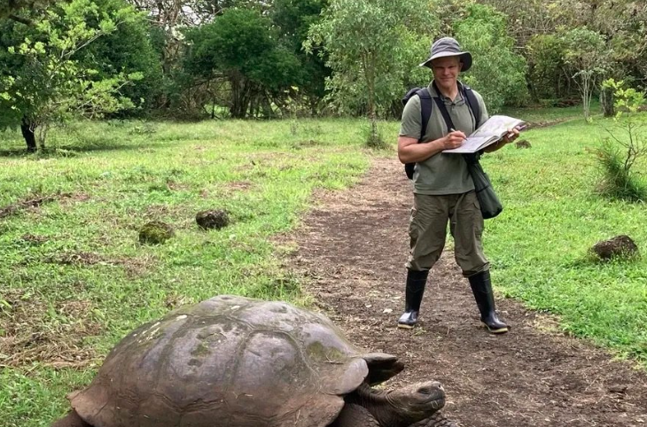 Joh Muir Laws stands in boots and a hat observing a great tortoise in front of him.