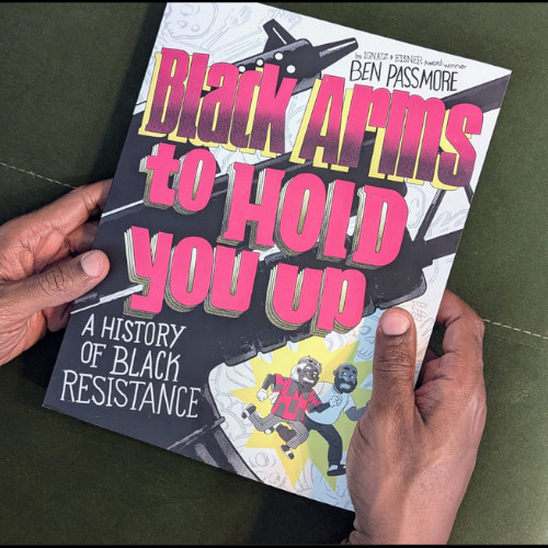 two hands holding the book "Black Arms To Hold You Up" featuring two cartoon figures running in the bottom corner and the words