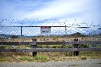 A field behind a chainlink fence with barbed wired and a sign that reads caution, keep out.