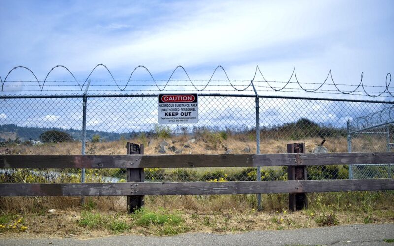 A field behind a chainlink fence with barbed wired and a sign that reads caution, keep out.