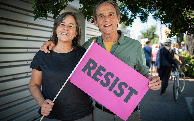 A man and a woman standing side by side holding a "Resist" sign