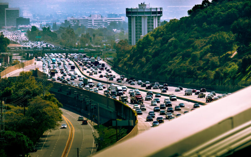 Cars in traffic on an urban freeway with green hills nearby.