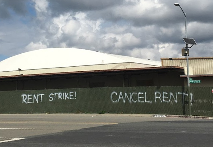 Spray paint on a fence in Oakland reads, rent strike, cancel rent