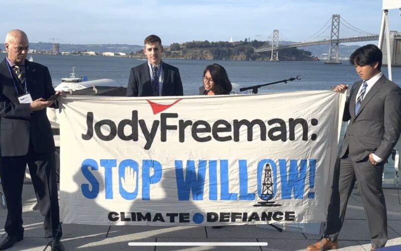 Four persons holding up a banner that says "Jody Freeman: Stop Willow." The Bay Bridge and SF Bay is visible in the background