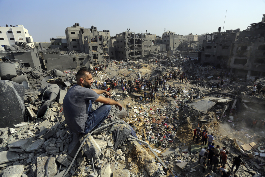 A man sits on the rubble as others wander among debris of buildings that were targeted by Israeli airstrikes in Jabaliya refugee camp, northern Gaza Strip, Wednesday, Nov. 1, 2023. A new U.N. report paints a stark picture of the devastating collapsing Palestinian economy after a month of war and Israel’s near total siege of Gaza. (AP Photo/Abed Khaled, File)