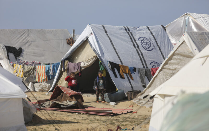 Palestinian children displaced by Israeli air and ground offensive on the Gaza Strip walk through a temporary tent camp near Kerem Shalom crossing in Rafah, Sunday, Jan. 14, 2024. (AP Photo/Hatem Ali)