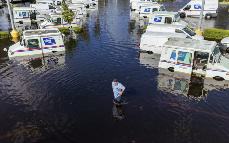 A USPS worker inspects trucks that had been relocated to protect them from wind but which are now underwater as intense rain from Hurricane Milton caused the Anclote River to flood, Friday, Oct. 11, 2024, in New Port Richey, Fla. (AP Photo/Mike Carlson)