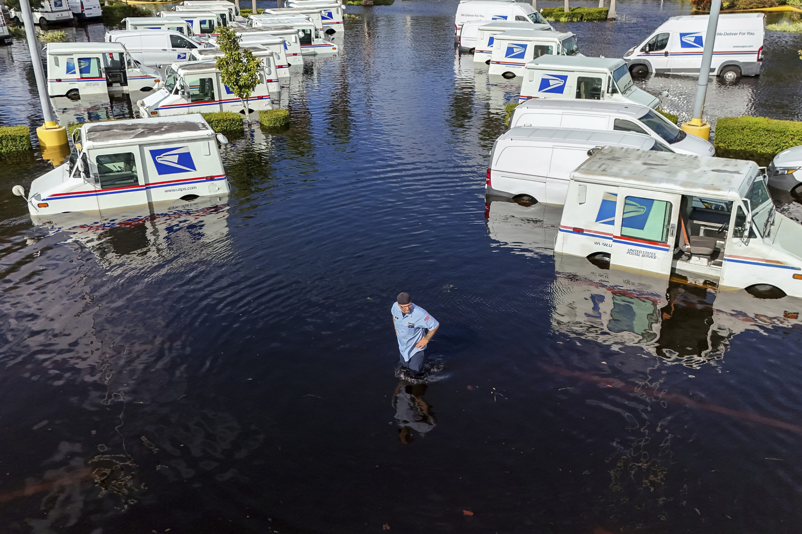 A USPS worker inspects trucks that had been relocated to protect them from wind but which are now underwater as intense rain from Hurricane Milton caused the Anclote River to flood, Friday, Oct. 11, 2024, in New Port Richey, Fla. (AP Photo/Mike Carlson)