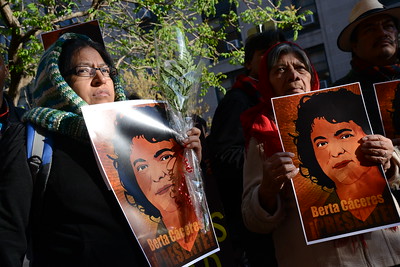 Two women hold identical posters with a photo of slain Honduran environmental activist and Indigenous leader Berta Cáceres at a vigil. The poster includes words in Spanish that say Honduran "Berta Cáceres is present."